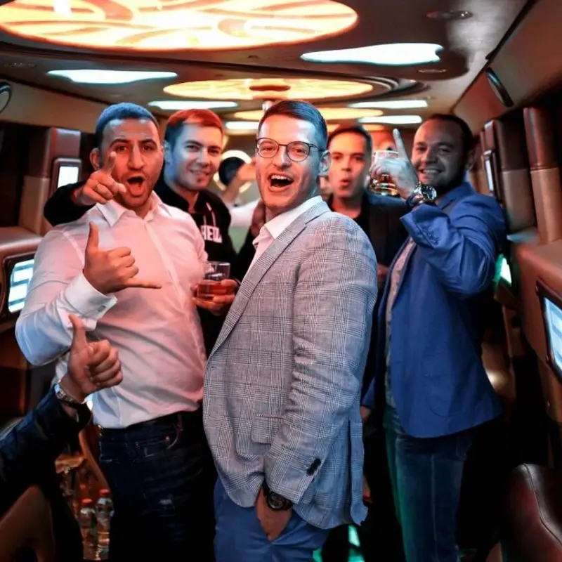 A group of enthusiastic men celebrating and gesturing inside a party bus with colorful lighting.