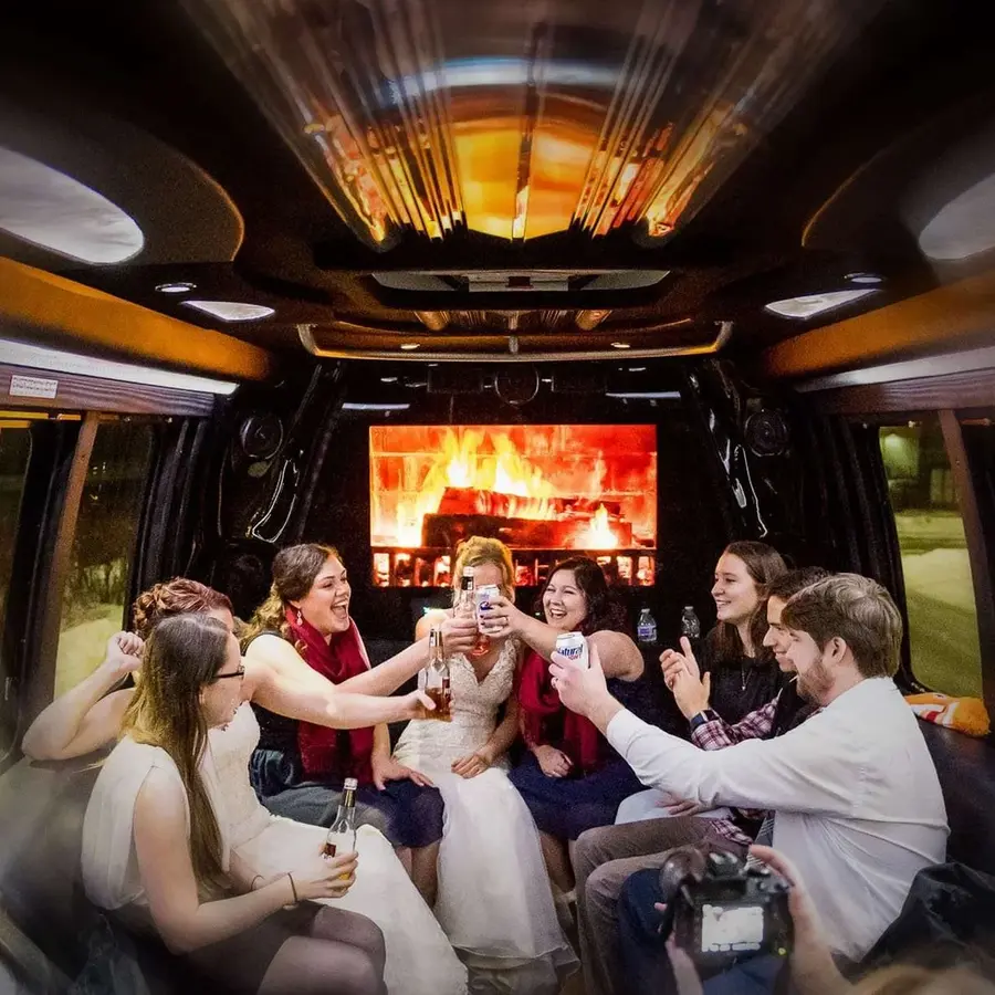Group event limo service A group of friends celebrates inside a luxury limousine with a fireplace display, raising their drinks for a toast.