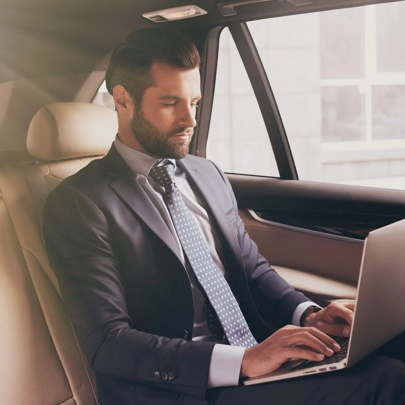 Professional Standard Car Service A businessman in a suit working on a laptop in the backseat of a luxury car.