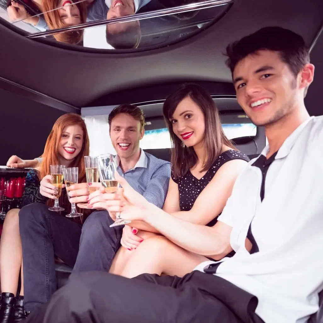 A group of four happy friends posing and toasting with glasses of sparkling wine inside a limousine.